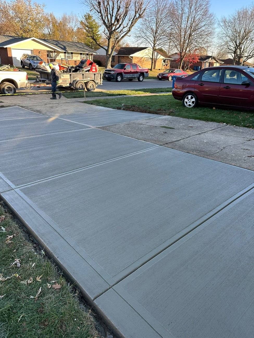 New broom finished concrete driveway meeting the street, with the crew and the Stallion trailer parked up the block