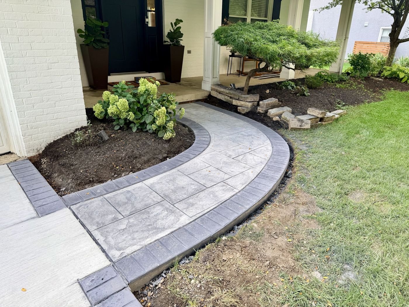Curved stamped concrete walkway with a darker border sweeping past hydrangeas to a dark front door