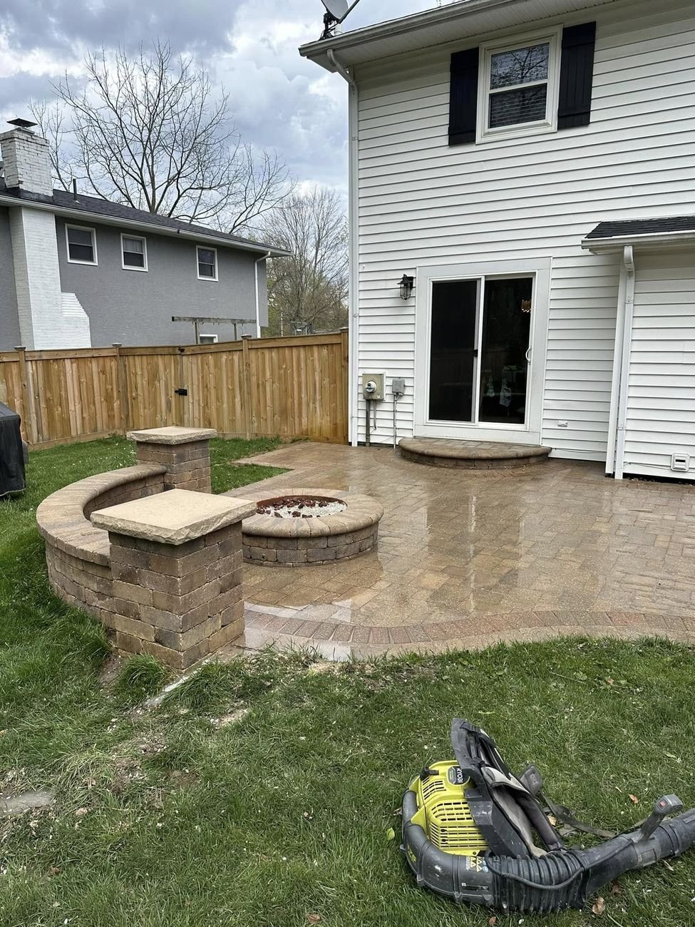 The cleaned patio still wet, the two capped columns and fire pit standing out against the green yard