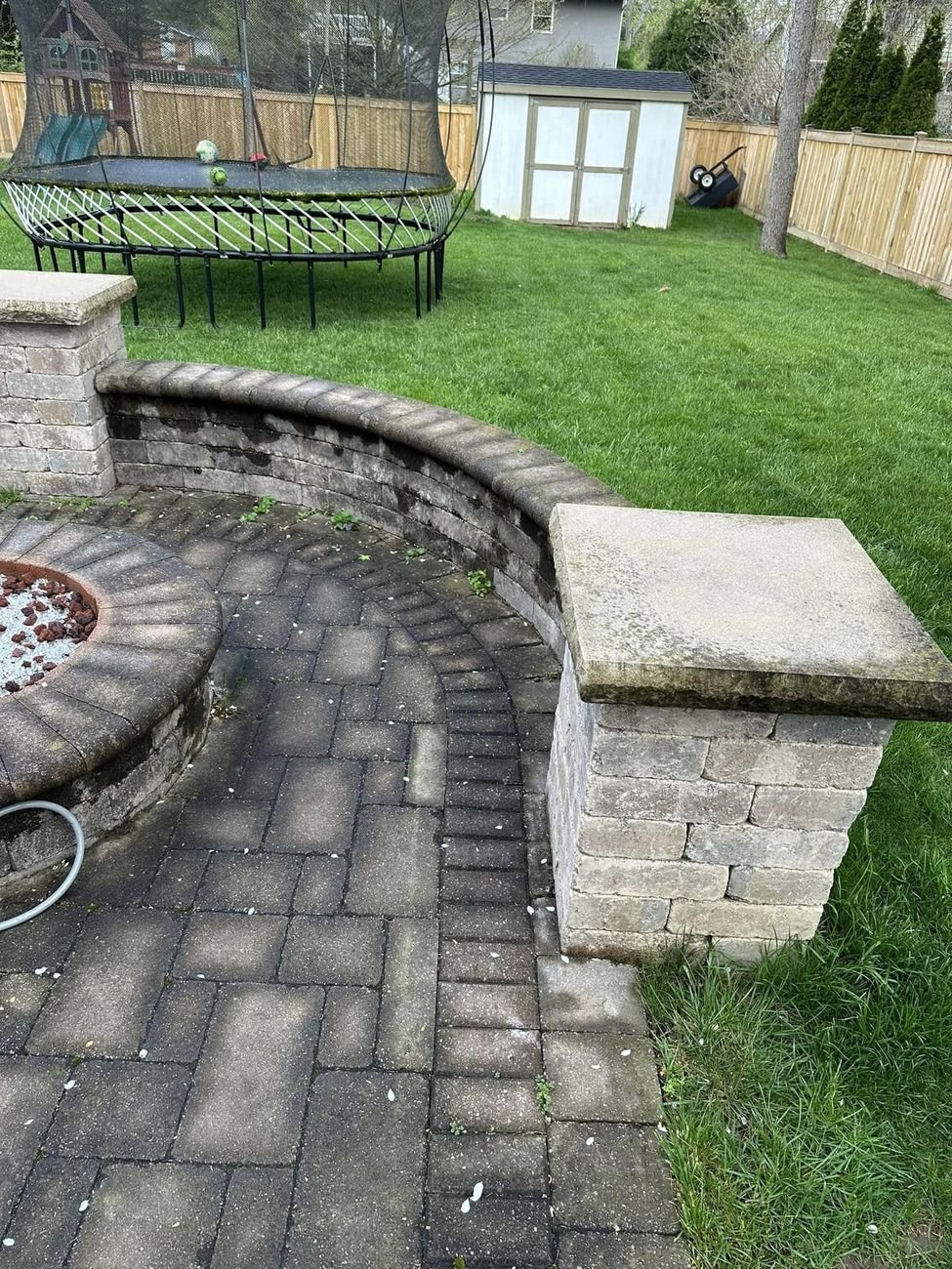 The curved seat wall and fire pit before washing, caps stained dark and weeds coming up in the joints