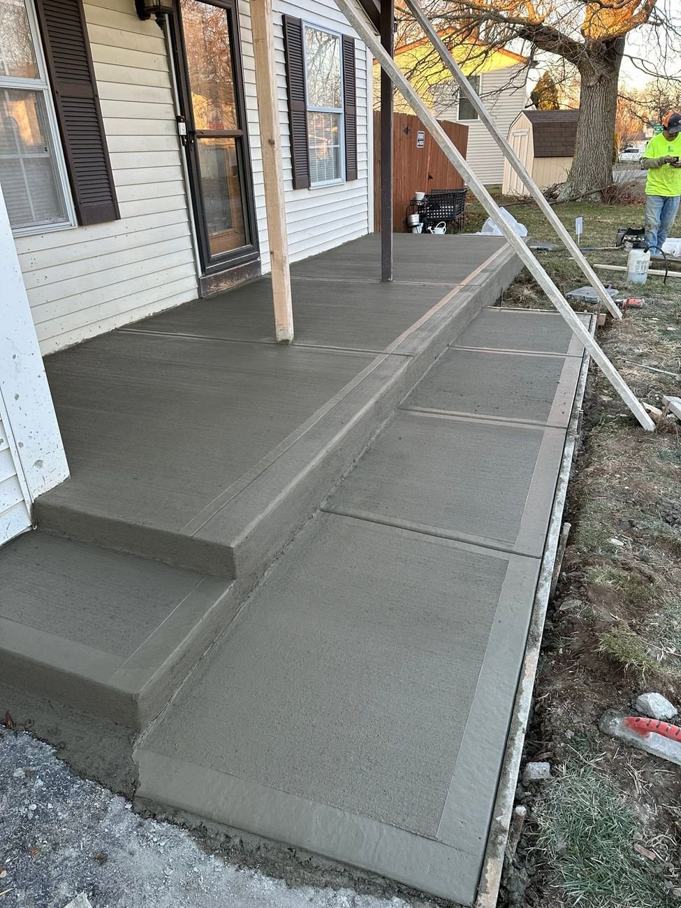 Freshly poured concrete porch, steps and walkway at dusk with a crew member finishing at the far end