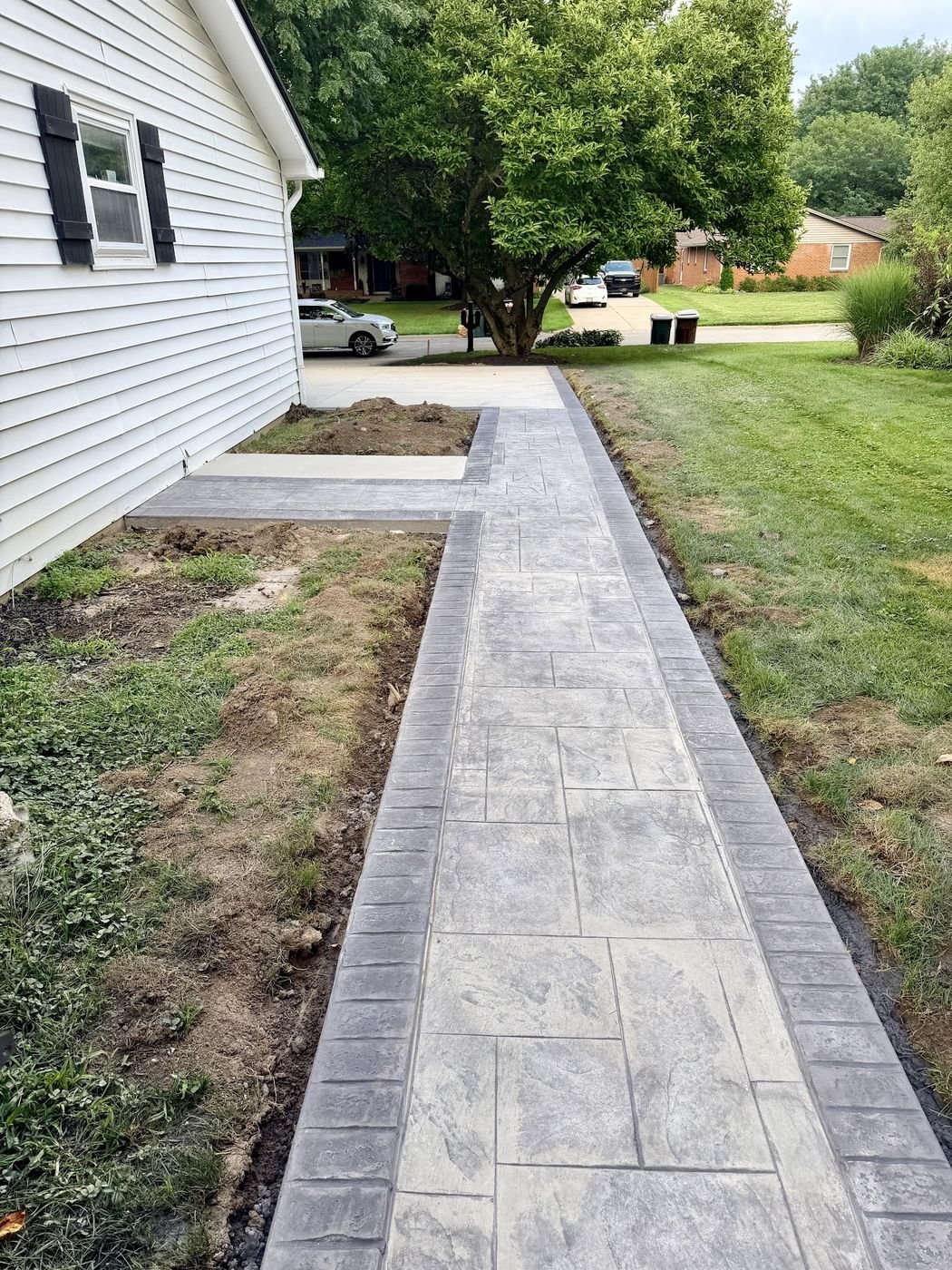 Stamped concrete walkway with a dark border running the length of the house out to the driveway
