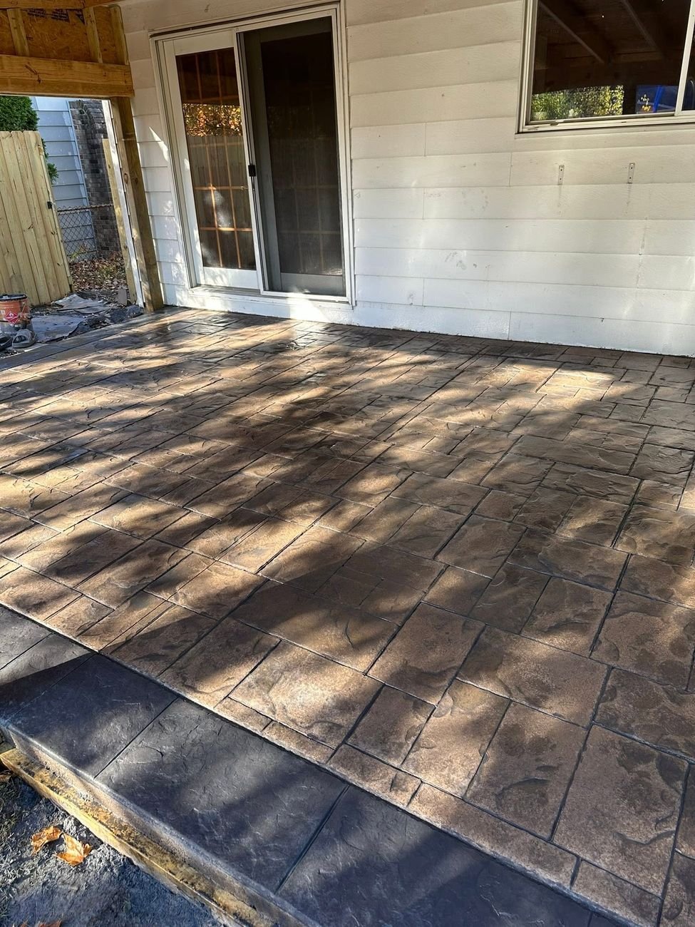 Warm brown stamped concrete patio in dappled shade running from a step up to a sliding door